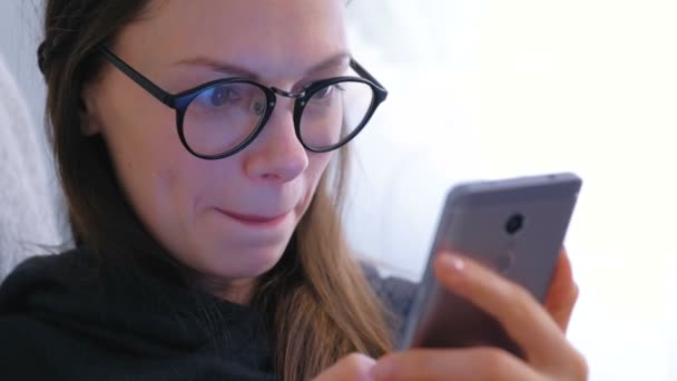 Jonge gelukkig brunette vrouw in glazen typt een bericht op een mobiele telefoon. — Stockvideo