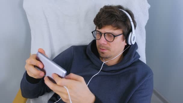 Muž v brýlích a sluchátka hrát hru v smartphone. Gamer relax. — Stock video