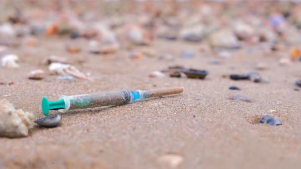 Medicinska sprutor bland rapan skalen i sanden på stranden efter storm. — Stockvideo