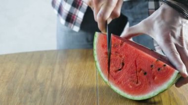 Adam karpuz mutfak masasının üzerinde küçük dilimler halinde keser. Eller yakın çekim.