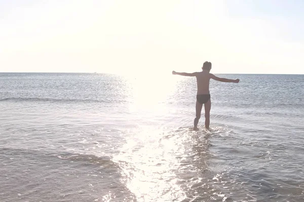 La silueta de niño está caminando por el agua del mar al atardecer. Nadar en el mar . —  Fotos de Stock