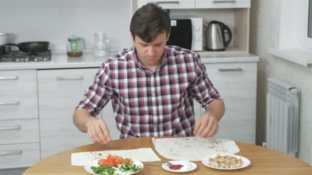 Чоловік готує інгредієнти для приготування шаурми на кухонному столі вдома. Піта, овочі та зелена цибуля з соусом та майонезом . — стокове відео