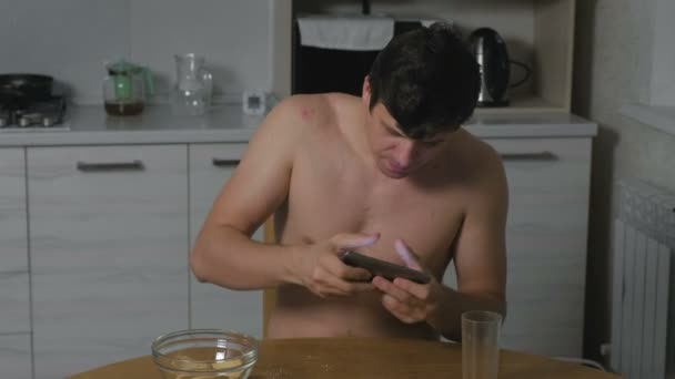 Mladý muž jí soubory cookie v kuchyni v noci a hraní her na telefonu. Nespavost a úzkost. Nadměrné jídlo. — Stock video