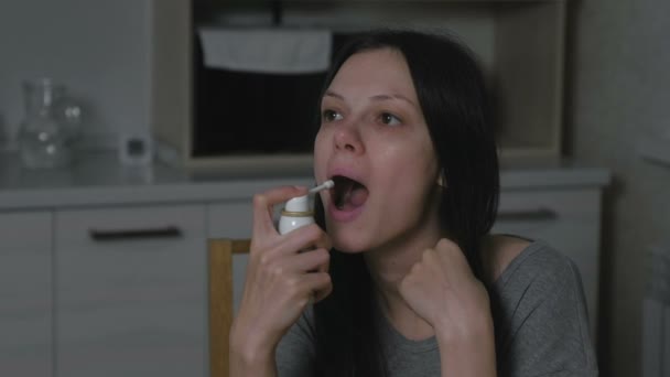 Zieke jonge vrouw met behulp van keel spray aërosol in de keuken bij nacht. Behandeling van verkoudheid thuis. — Stockvideo