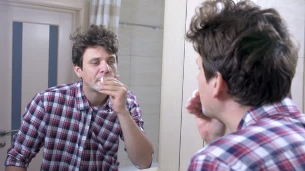 Mann im karierten Hemd mit Kater rasiert sich beim Blick auf Spiegel im Badezimmer. — Stockvideo