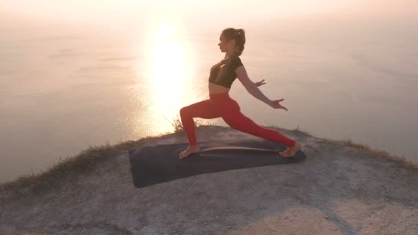 Schöne Ansicht der Frau beim Yoga einbeinige nach unten gerichtete Hundehaltung, High Lunch Pose auf dem Berg mit Meerblick bei Sonnenuntergang. — Stockvideo