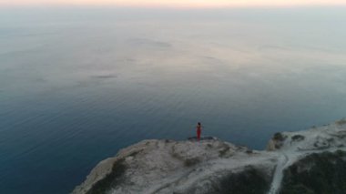 Güzel kadın yoga stretcing ve gün batımında deniz manzaralı dağ üstüne meditasyon yapıyor. Havadan görüntüleri. Arkadan görünüm.