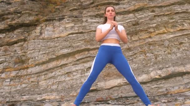 Chica haciendo sentadilla embestir el bodyflex durante los ejercicios de respiración en el fondo de roca . — Vídeos de Stock