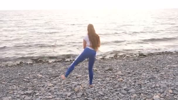 Meisje doet oefening longe, been heffen de bodyflex tijdens de ademhalingsoefeningen op de achtergrond van de zee. — Stockvideo