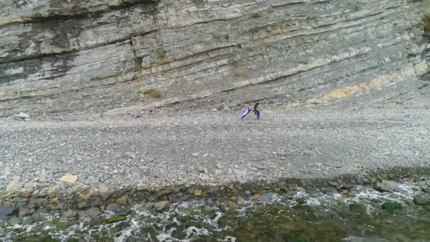 女性には、ヨガ ・岩と海の背景に物理的な演習を行っています。空中の美しい映像表示. — ストック動画
