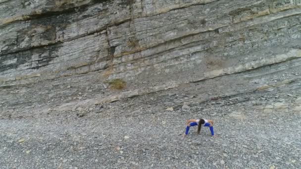 在岩石背景下的呼吸练习中, 妇女正在做蹲和伸展身体弯曲。空中美丽的画面视图. — 图库视频影像