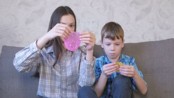 Szczęśliwa mama i syn grają z śluzu, siedząc na kanapie. Rozciąganie zamulać patrząc przez szlam. — Wideo stockowe