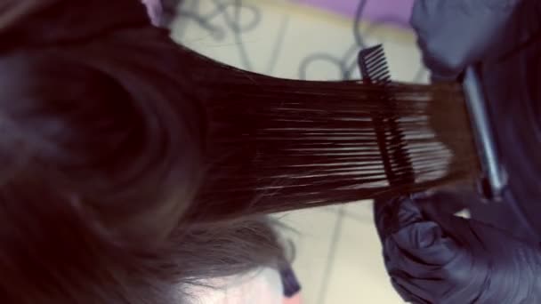 Parrucchiere lisci capelli castani scuri di bella donna utilizzando pinze per capelli nel salone di bellezza. Primo piano dei capelli . — Video Stock