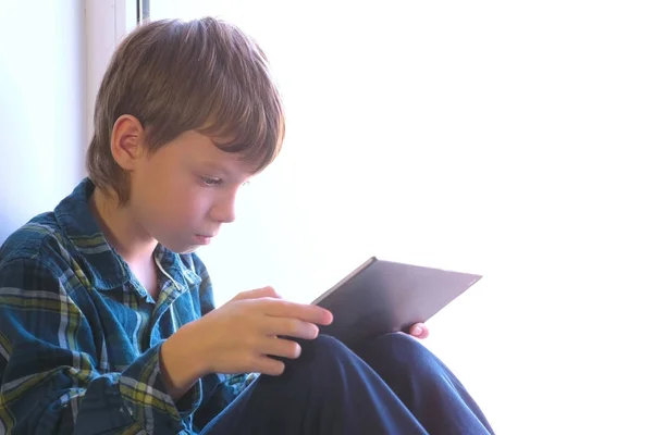 Glücklicher Junge spielt auf Fensterbank in Tablet-Computer. — Stockfoto