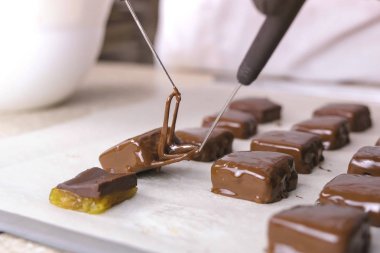 Baker eritilmiş çikolata şekerler dips ve kurumaya baker kağıt üzerine koydu. Çikolata şekerleme üretimi. Eller yakın çekim.