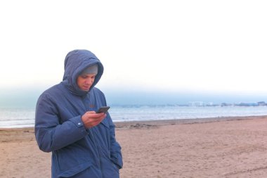 Bir cep telefonu ile deniz kenarında plajda bir ceketli adamı. Kış deniz.