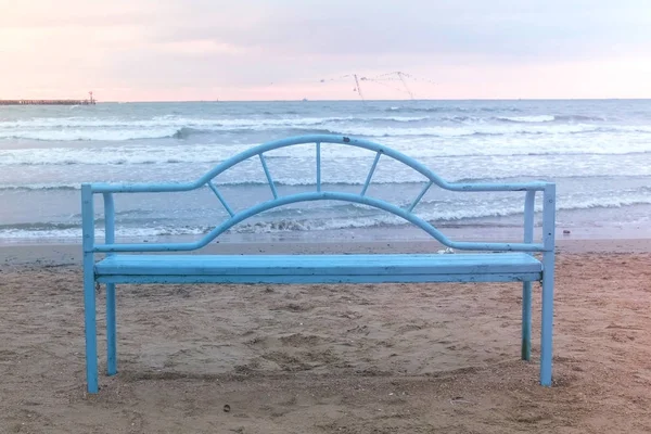 Banco azul na praia ao pôr-do-sol. Infra-estrutura conveniente para relaxar à beira-mar. Onda marítima . — Fotografia de Stock