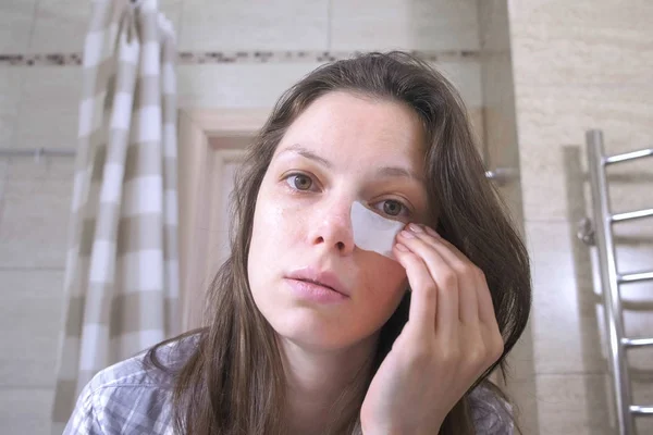 Cansada mulher acordada com uma ressaca coloca manchas nos olhos no banheiro . — Fotografia de Stock