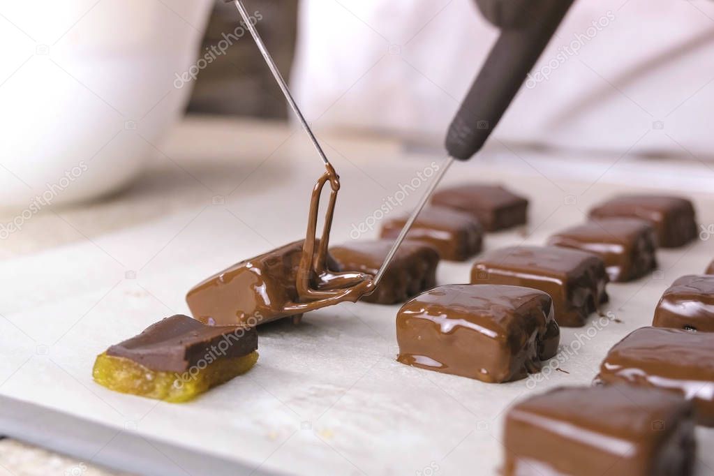 Baker dips candies in melted chocolate and put it on baker paper to dry. Production of chocolate candies. Hands close-up.