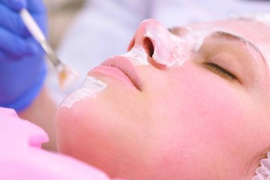Güzellik uzmanı fırça ile kadının yüzünde maske koyar. Yüz nemlendirici. Yüz yakın çekim.