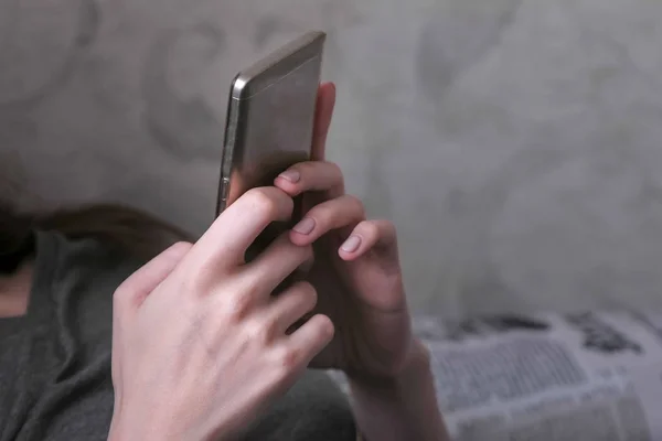 Mujer acostada en el sofá y leyendo algo en el teléfono móvil. Primer plano manos con teléfono . — Foto de Stock