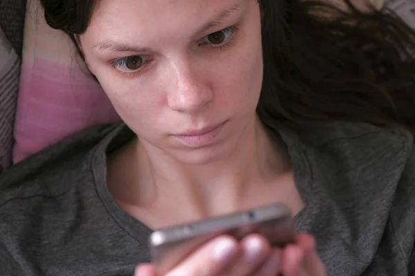 Mujer acostada en el sofá y leyendo algo en el teléfono móvil. Cara de primer plano . — Foto de Stock