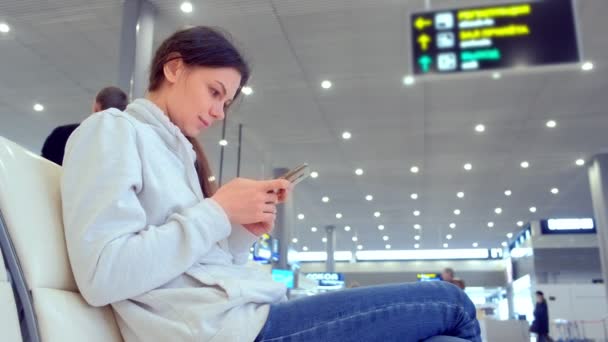 Registro de mujer en línea en su teléfono móvil en la sala del aeropuerto, vista lateral . — Vídeos de Stock