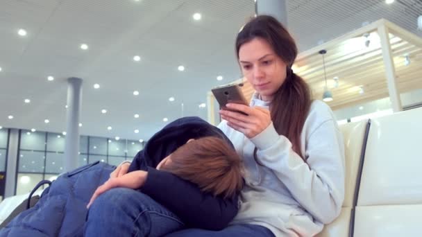Женщина со своим уставшим сыном зарегистрировалась онлайн на свой мобильный телефон в зале аэропорта . — стоковое видео