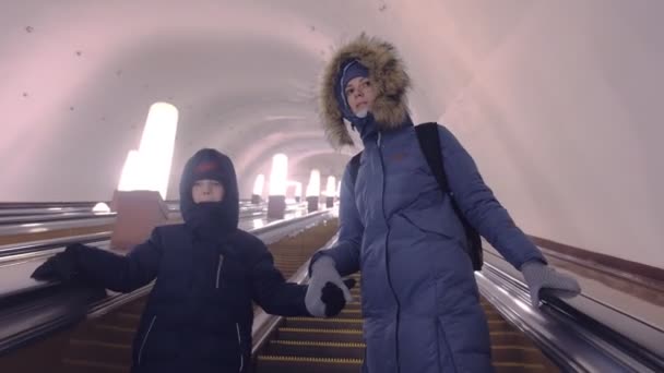 穿着冬装的妈妈和儿子正在地铁隧道的自动扶梯上移动. — 图库视频影像
