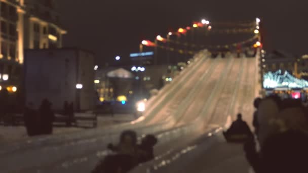 La gente monta en toboganes de hielo en tuberías por la noche en la ciudad, borroso . — Vídeo de stock