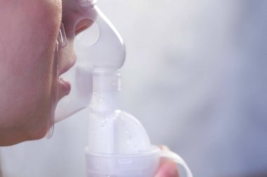 Nebulizatör ve astım tedavisi için kullanın. Genç kadın inhaler maskesi teneffüs edilmesi. Yakın çekim burun ve dudaklarını maskesindeki, yan görünüm.