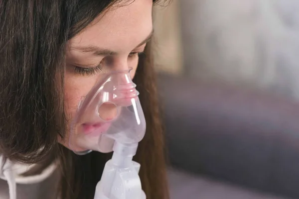 Use nebulizer and inhaler for the treatment. Young woman inhaling through inhaler mask, face close-up.