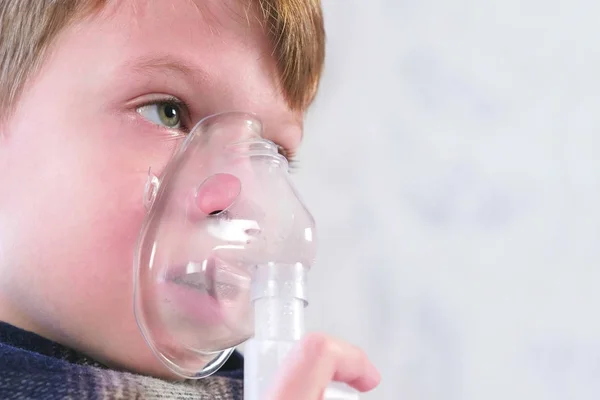 Sick boy inhaling through inhaler mask, face close-up side view. Use nebulizer and inhaler for the treatment.