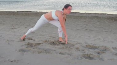 Genç kadın kum plajındaki yoga yaparken güneş doğarken.
