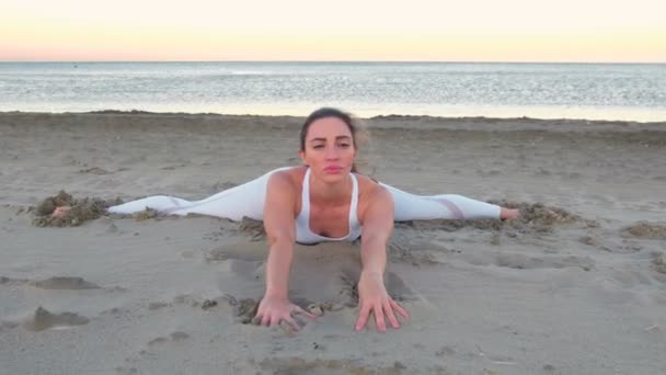 Mujer joven haciendo yoga estirándose sentada en frente se divide en la playa de arena al amanecer . — Vídeos de Stock