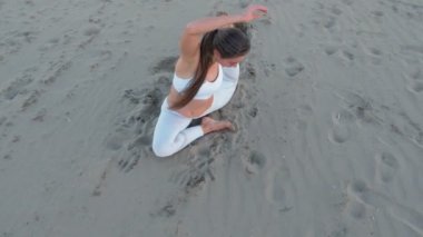 Genç kadın yoga güvercin poz kumlu plajda güneş doğarken yapıyor.