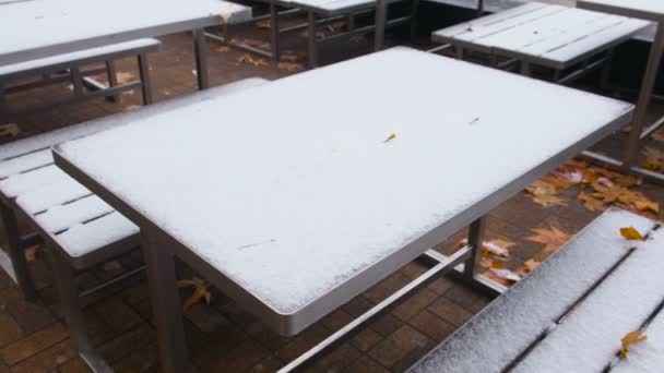 Pokryte śniegiem stoły i ławki w parku jesienią żółte liście. — Wideo stockowe
