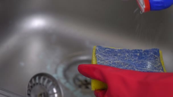 Vrouw wast een metalen spoelbak met spons in de keuken in rode handschoenen. Close-up van de handen. — Stockvideo