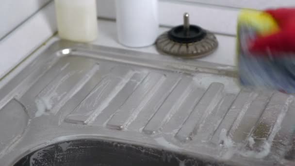 Vrouw wast een metalen spoelbak met spons in de keuken in rode handschoenen. Close-up van de handen. — Stockvideo