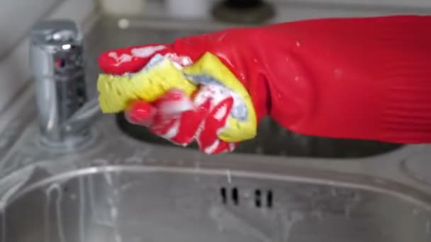 Femme lave un robinet en métal avec éponge dans la cuisine avec des gants rouges. Gros plan des mains . — Video