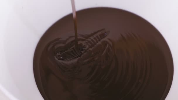 Gießt flüssige dunkle Schokolade in eine weiße Schüssel. Nahaufnahme. — Stockvideo