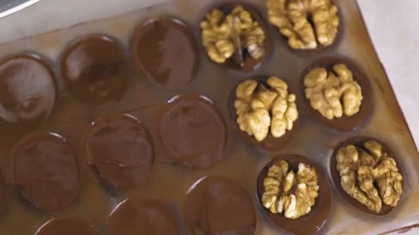 Bagare händer lägga halvorna av valnötter på choklad godis i formulären. — Stockvideo