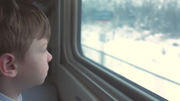 Хлопчик дивиться у вікно в рухомому поїзді на зимовому пейзажі . — стокове відео