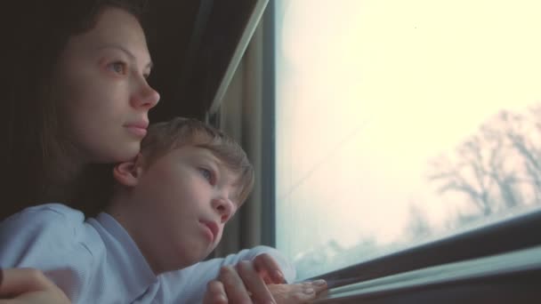 Moe moeder en zoon zoekt in venster in bewegende trein op winterlandschap. — Stockvideo