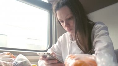 Yorgun kadın smartphone üzerinde şehirlerarası bir tren seyahat eden bir kitap okuyor.