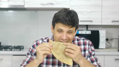 Yorgun genç adam ekose gömlekli bir iştah ve içecekler büyük bir cheburek yiyor.