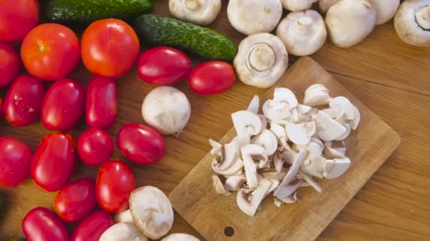 Snijden paddestoelen champignons op houten plank op de keukentafel met verschillende groenten. — Stockvideo