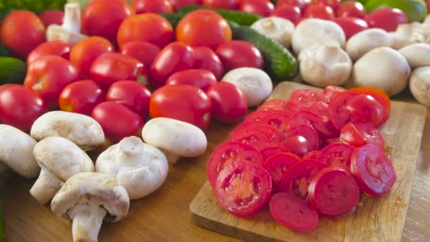 Vista de perto de legumes frescos e tomates de corte em tábua de madeira na mesa da cozinha. Vista lateral . — Vídeo de Stock