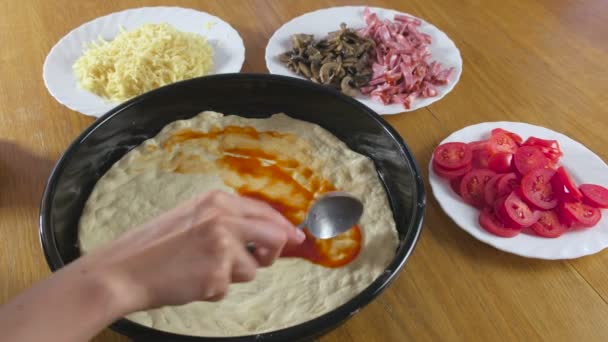 Κάνοντας μια πίτσα. Γυναικεία χέρια κάνουν μια σπιτική πίτσα. Σάλτσα ντομάτας με επάλειψη σε μια ζύμη. — Αρχείο Βίντεο