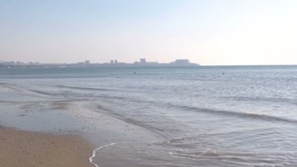 Praia de areia com ondas ao pôr do sol com vista para a cidade costeira . — Vídeo de Stock